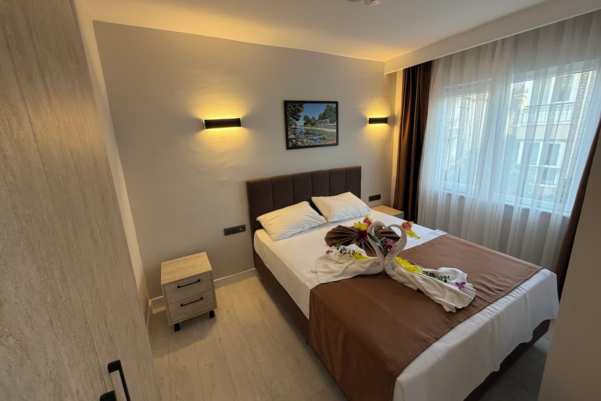 Ein Hotelzimmer mit Bett, Nachttischen, einem Wandbild und einem Fenster mit Vorhängen.