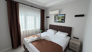 Habitación de hotel con una cama grande, cortinas marrones, un equipo de aire acondicionado, un cuadro en la pared y una mesita de noche.