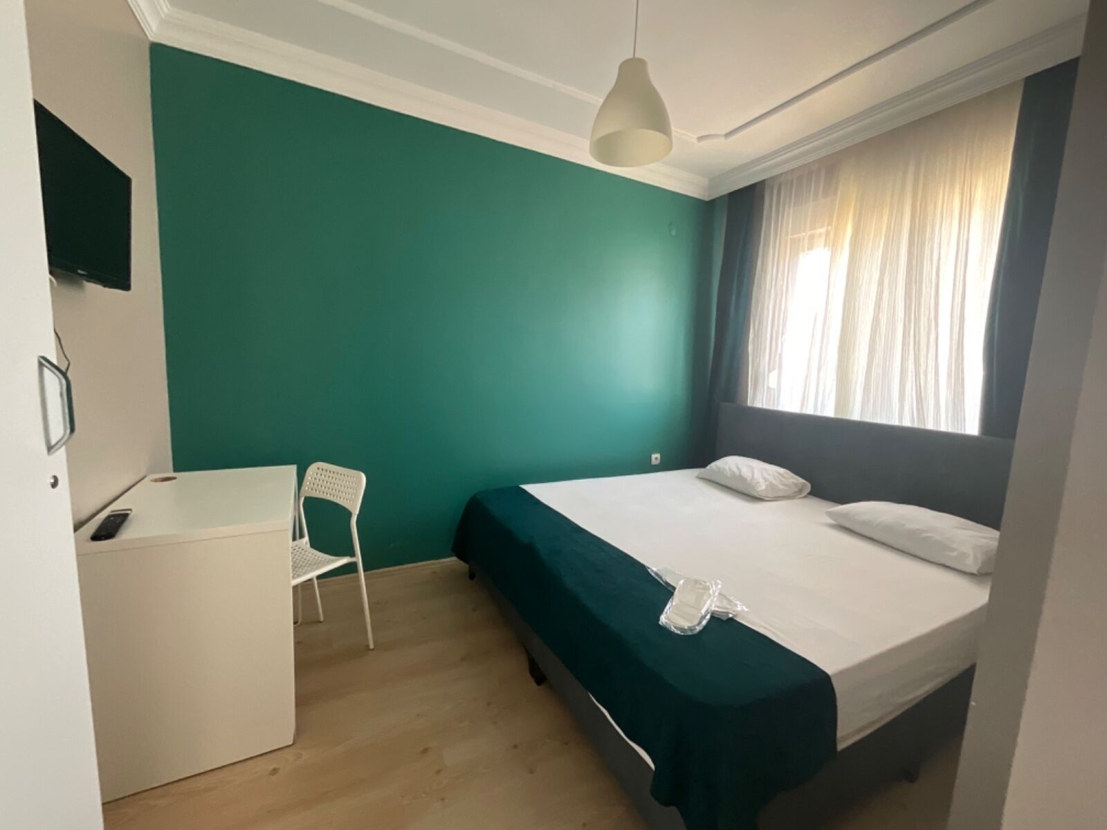 A bedroom with a bed, a desk, a chair, and a window with curtains.