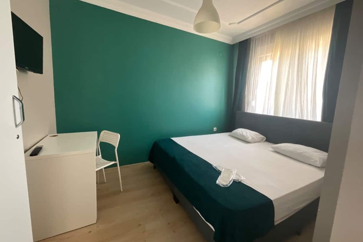 Ein Schlafzimmer mit einem Bett, einem Schreibtisch, einem Stuhl und einem Fenster mit Vorhängen.