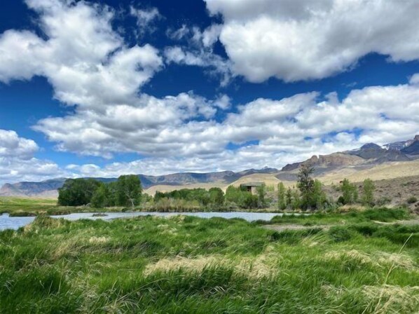 Un paisaje montañoso con un río, hierba verde y un pequeño edificio.