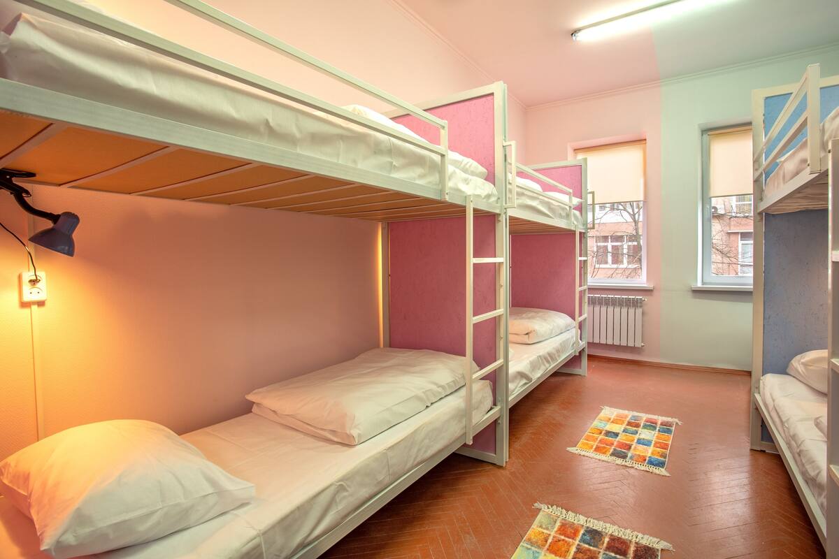 A dormitory room with bunk beds, a small window, and a radiator.