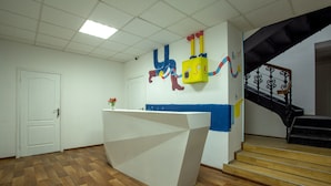 Zona de recepción de hotel con un mostrador moderno, una escalera y una pared decorada con arte colorido.