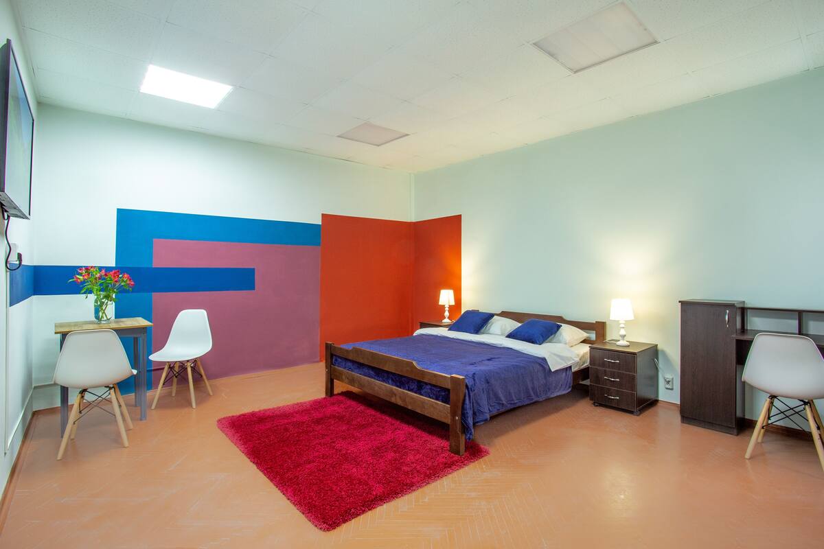 A bedroom with a bed, bedside tables, chairs, a desk, and a red rug.