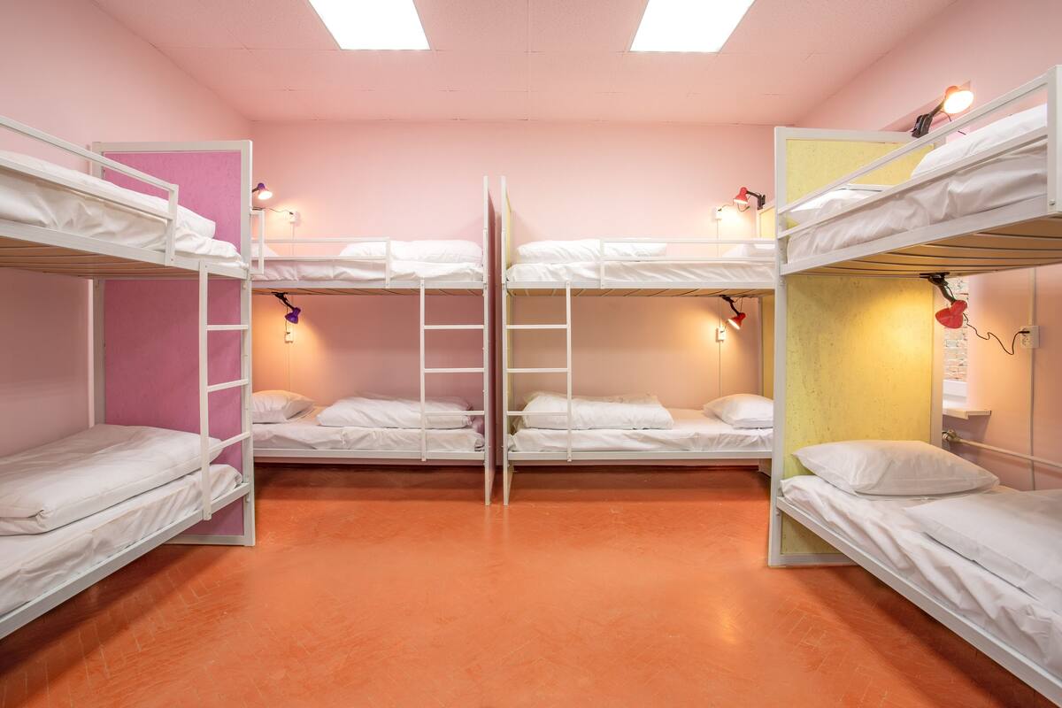 A dormitory room with bunk beds, a pink wall, and orange flooring.
