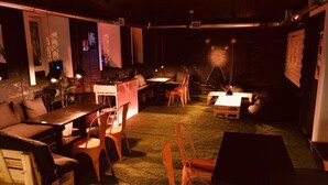 Un espacio interior acogedor con mesas y sillas, un escenario con equipo musical y una pared de ladrillo.
