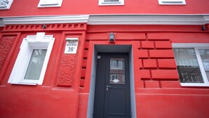 Un edificio rojo con puerta negra, marcos de ventana blancos y un cartel sobre la puerta.