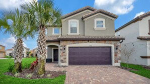 A two-story house with a stone facade, a dark garage door, and a well-maintained lawn with palm trees. - Private Pool Home w/Incredible Game Room! FREE Resort Access (Davenport)