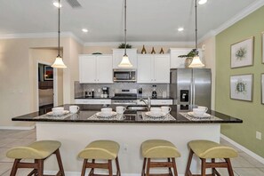 A modern kitchen with white cabinets, a central island with bar stools, stainless steel appliances, and pendant lighting.