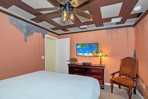 A bedroom with a bed, a ceiling fan, a TV, a lamp, a dresser, and a chair.