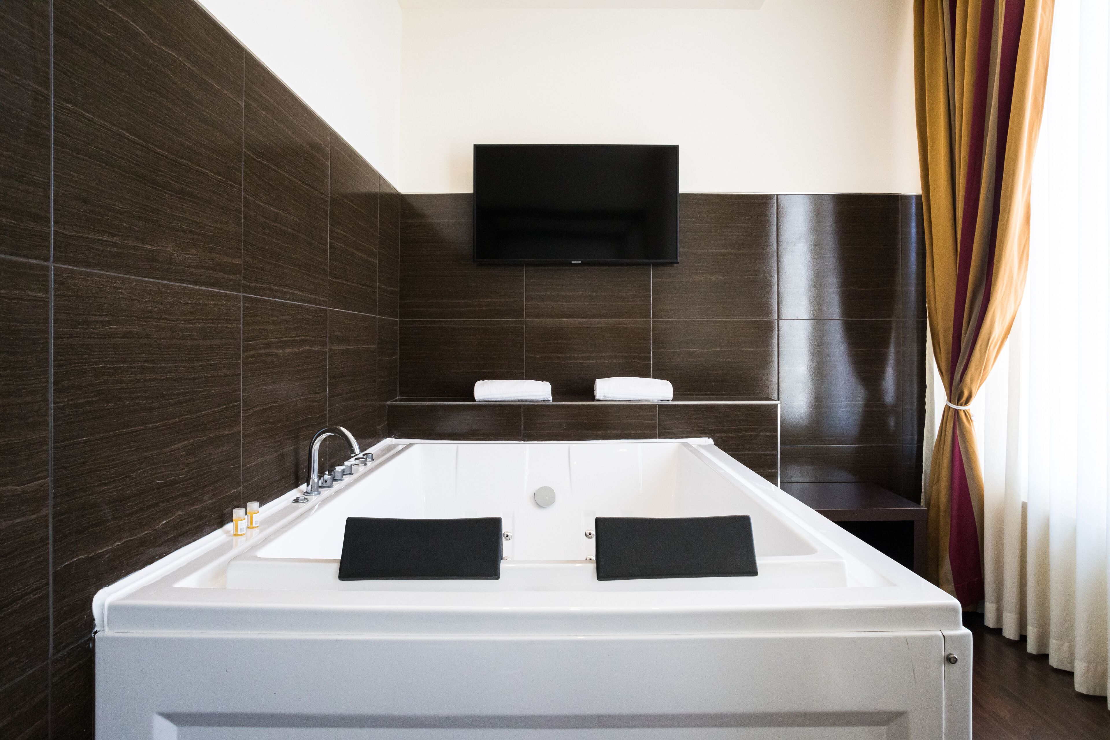Ein modernes Badezimmer mit einer großen Badewanne, einem an der Wand montierten Fernseher und einem Handtuchhalter.