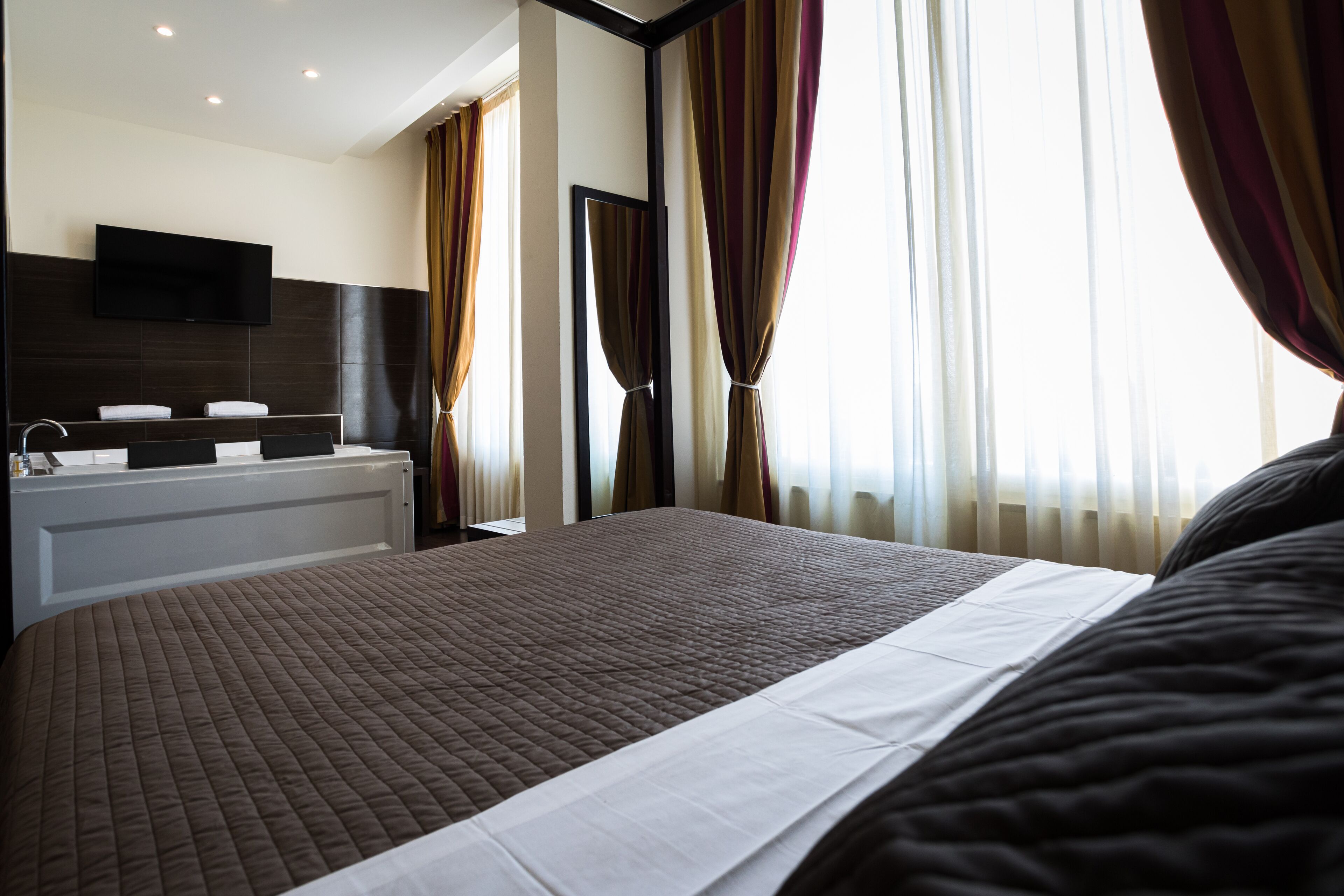 Une chambre d’hôtel avec un grand lit, un téléviseur intégré, une baignoire et des rideaux.