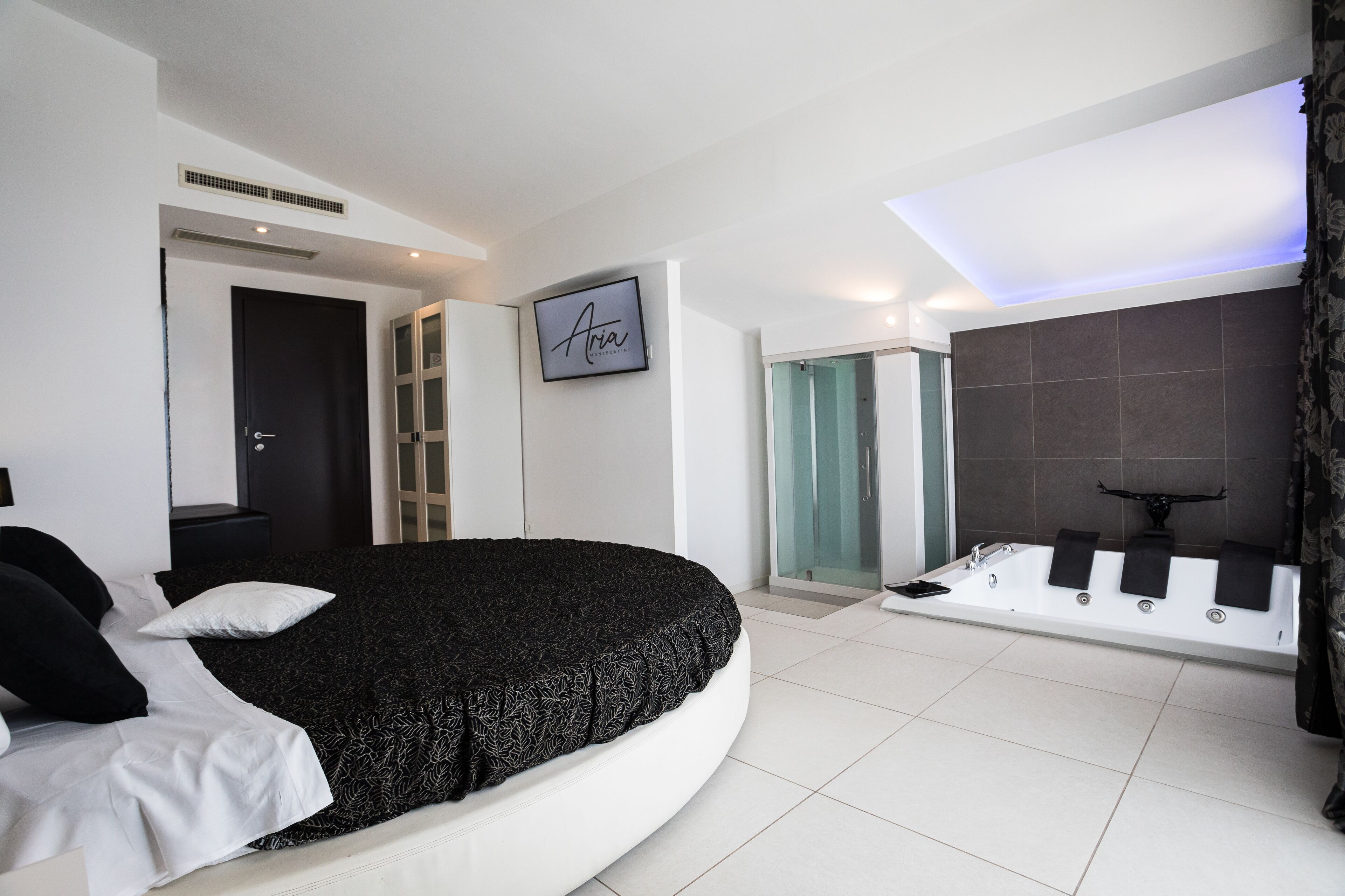 Une chambre à coucher moderne avec un lit aux lignes courbes, une douche en verre et une grande baignoire.