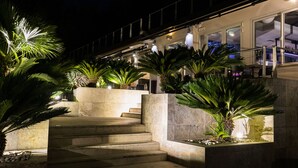 A well-lit outdoor area with steps leading to a building, surrounded by large potted plants and a stone wall. - La Villa Resort (Pieve a Nievole)