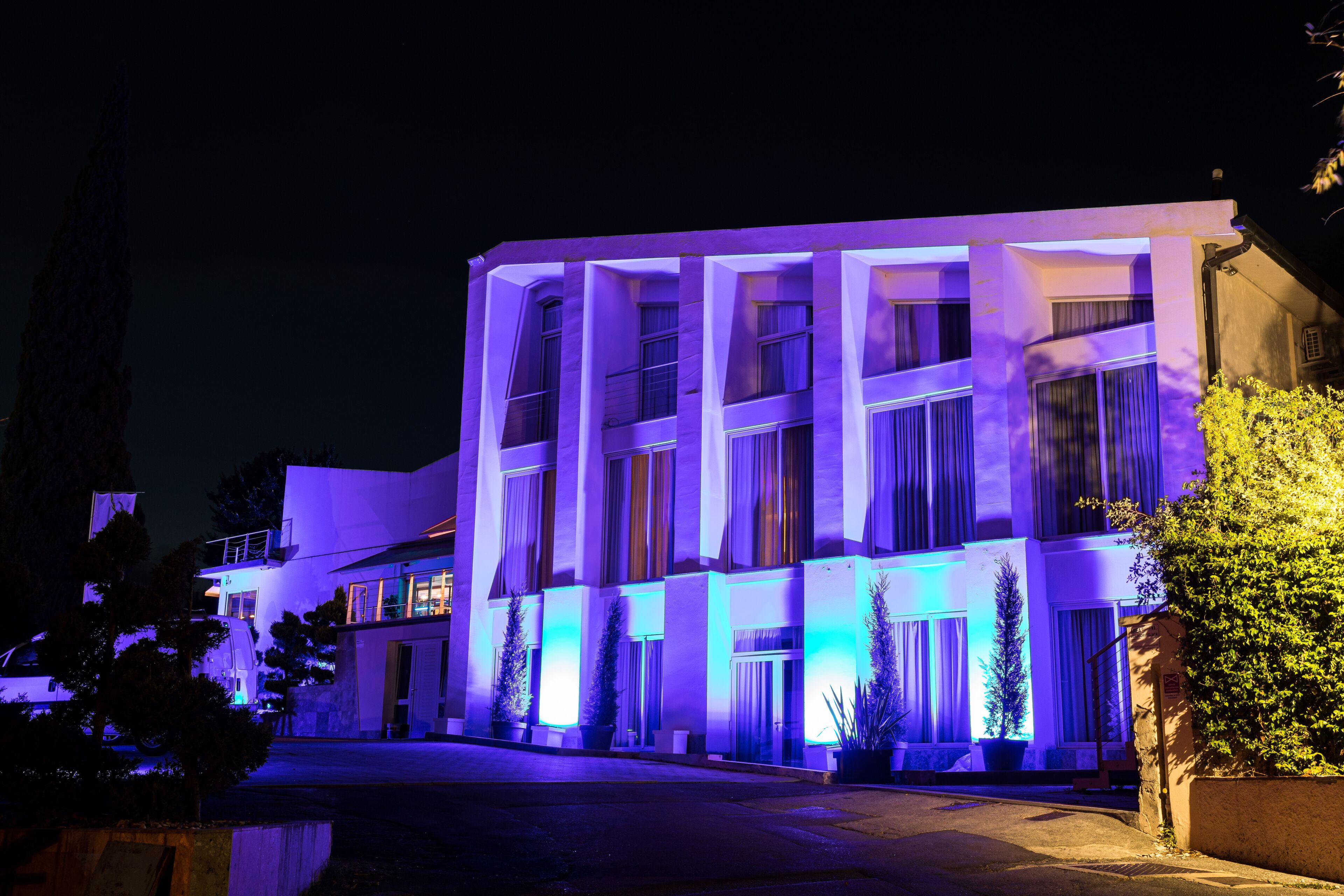Ein modernes Gebäude mit mehreren Stockwerken und großen Fenstern, beleuchtet mit violettem Licht.