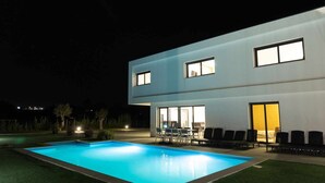 Un bâtiment moderne à deux étages doté d’une piscine, d’un espace extérieur aménagé et de grandes fenêtres.