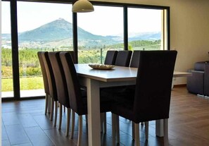 Un comedor con una mesa y sillas, ventanas amplias con vista a la montaña y una lámpara colgante.
