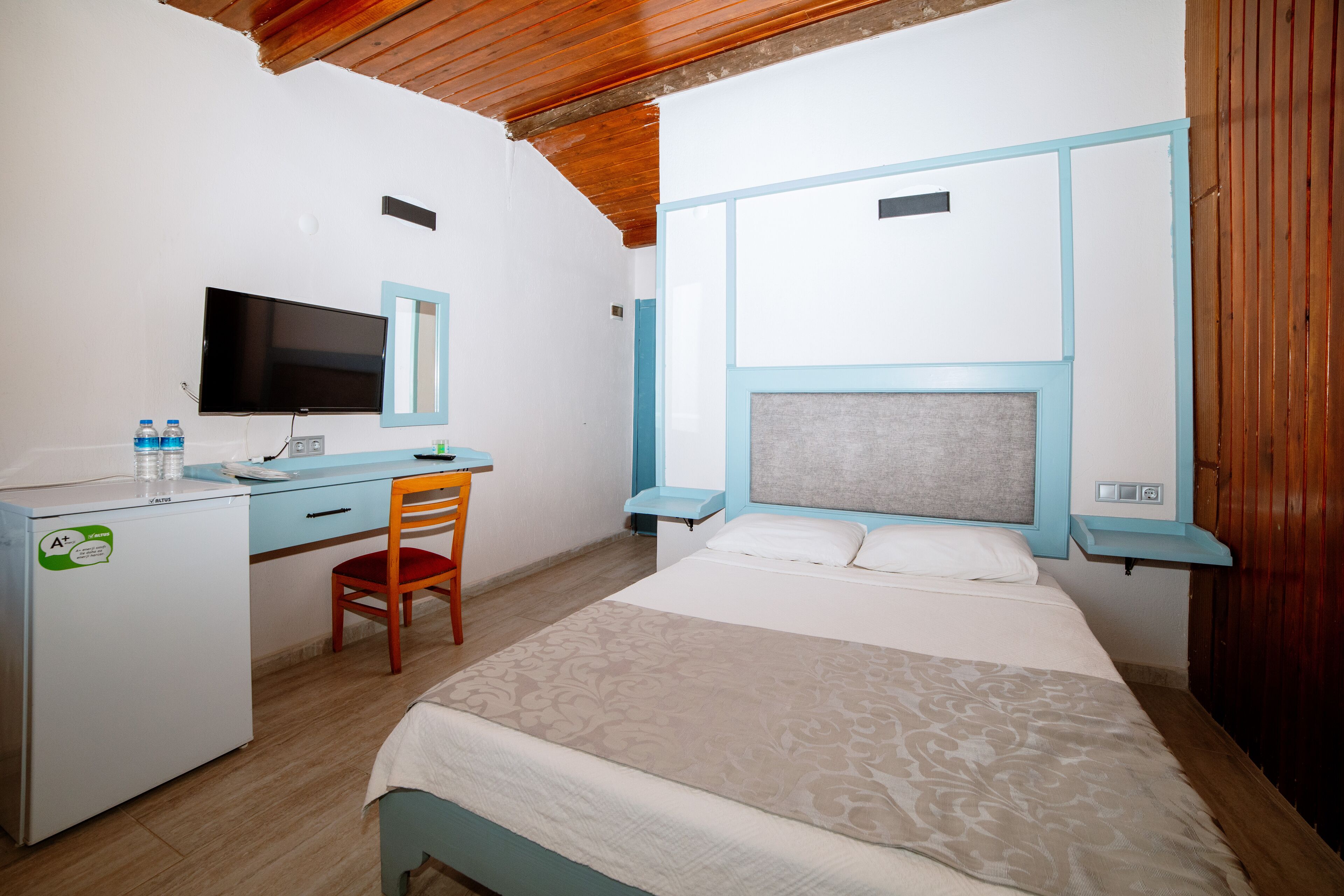 Un dormitorio con cama, escritorio, silla, televisor y un refrigerador pequeño.