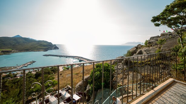 Un balcon offrant une vue sur une zone côtière, notamment une jetée et un terrain rocheux.