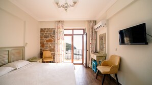 Une chambre à coucher comprenant un lit, deux chaises, un bureau, une télévision et un balcon avec un mur en pierre.