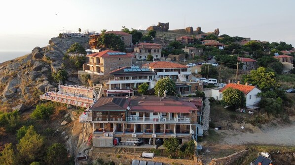 A coastal town with stone buildings, a prominent hotel with a red roof, and a rocky shoreline.