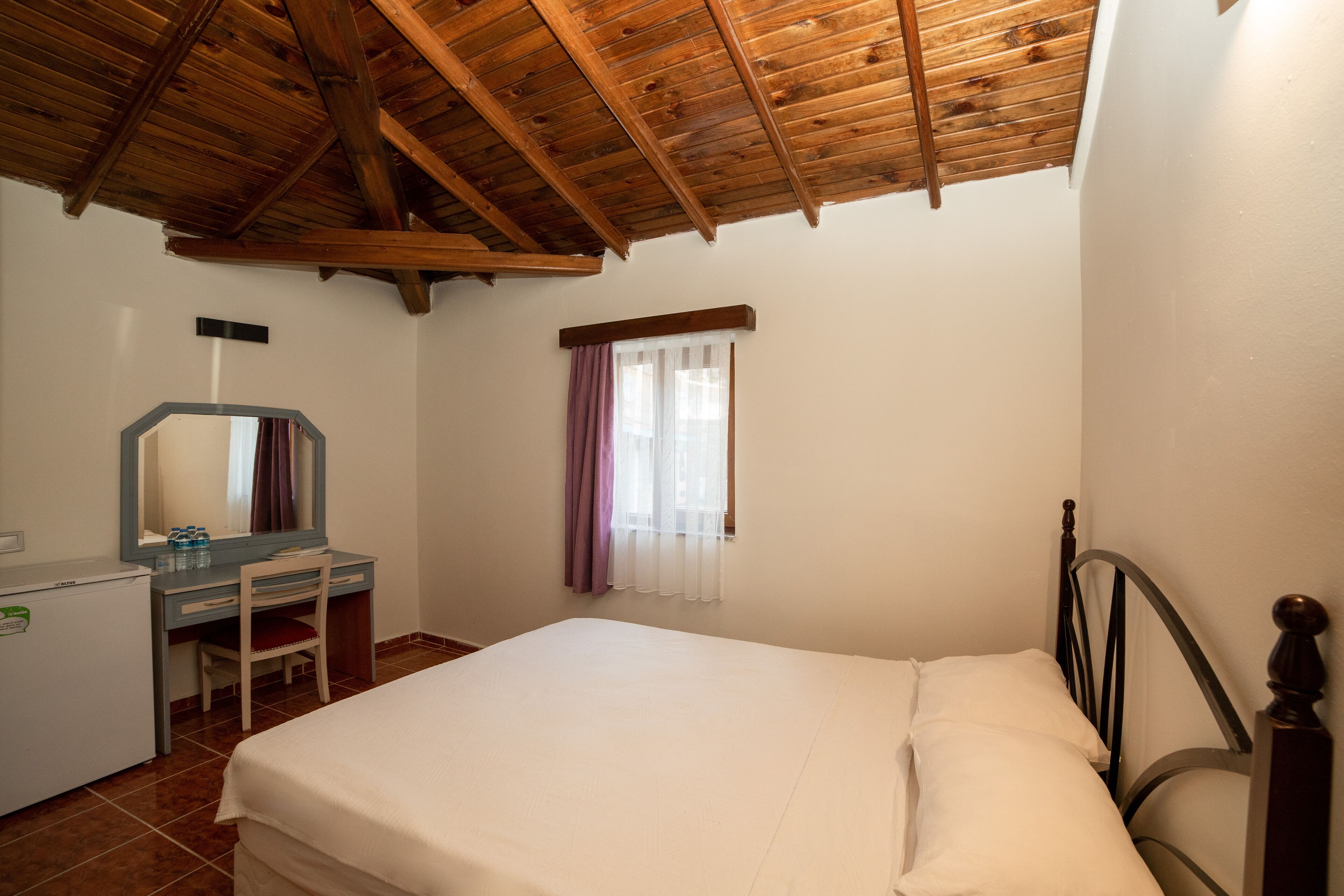 Un dormitorio con techo de madera, una cama, un escritorio con espejo y una ventana con cortinas.
