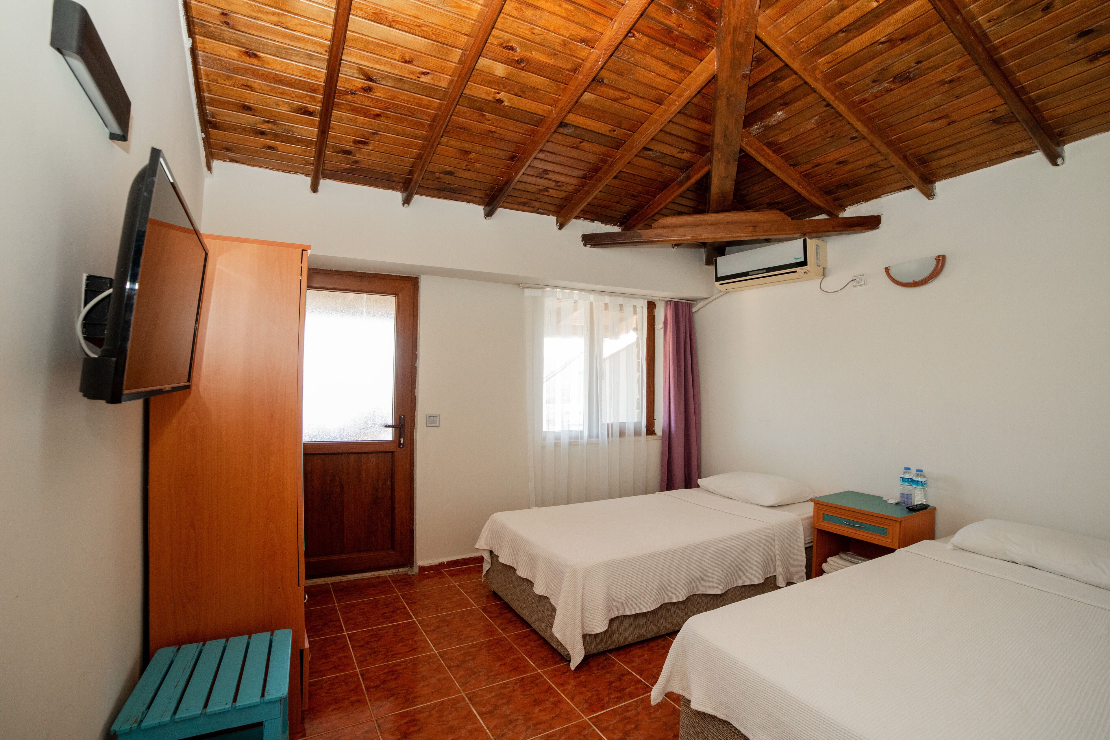 Habitación con dos camas, techo de madera, televisor en la pared y una mesita con una botella de agua.