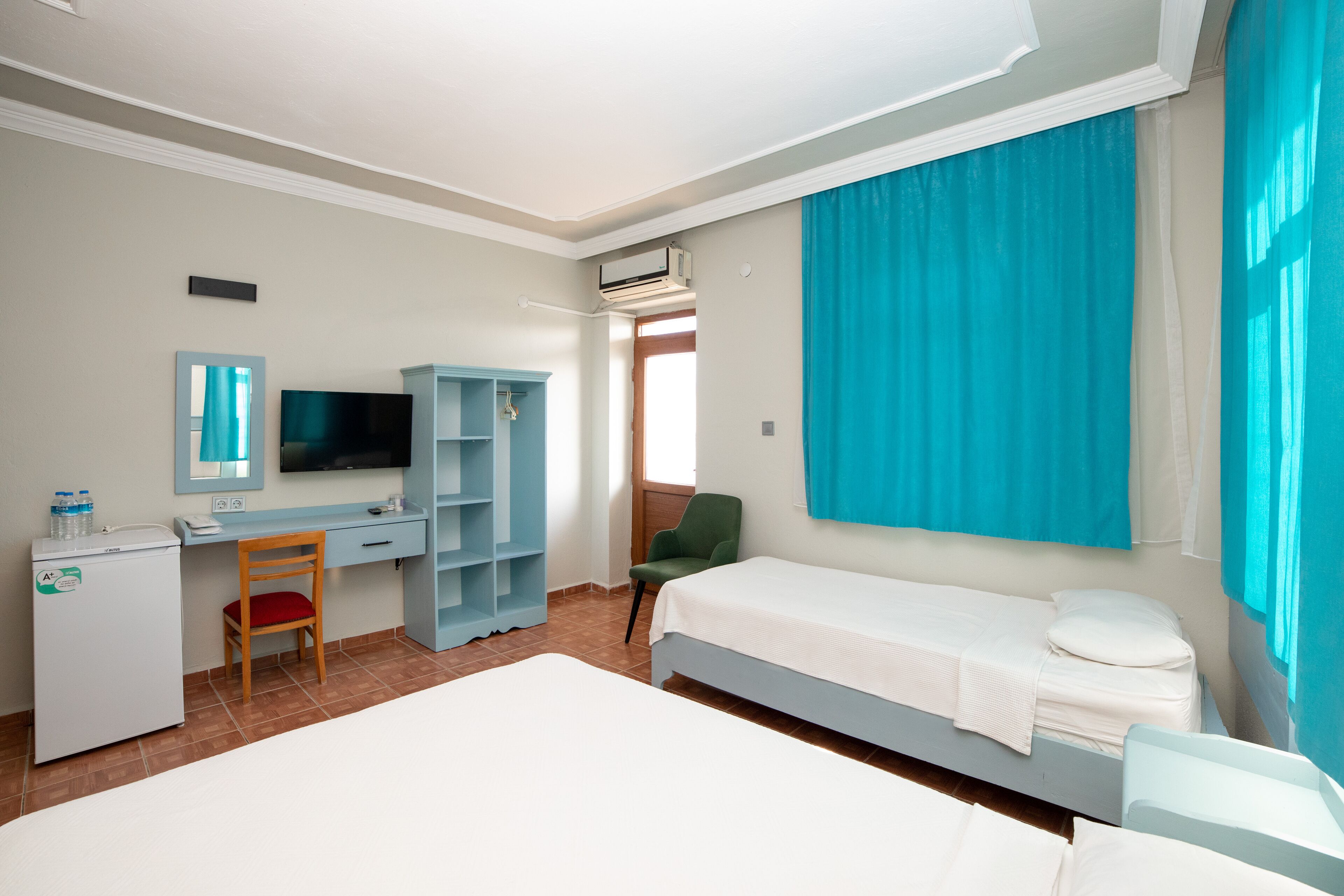 A hotel room with a bed, a desk with a chair, a television, and a wardrobe.