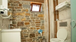 Une salle de bain avec un mur en pierre, une fenêtre, des toilettes et un porte-serviettes.