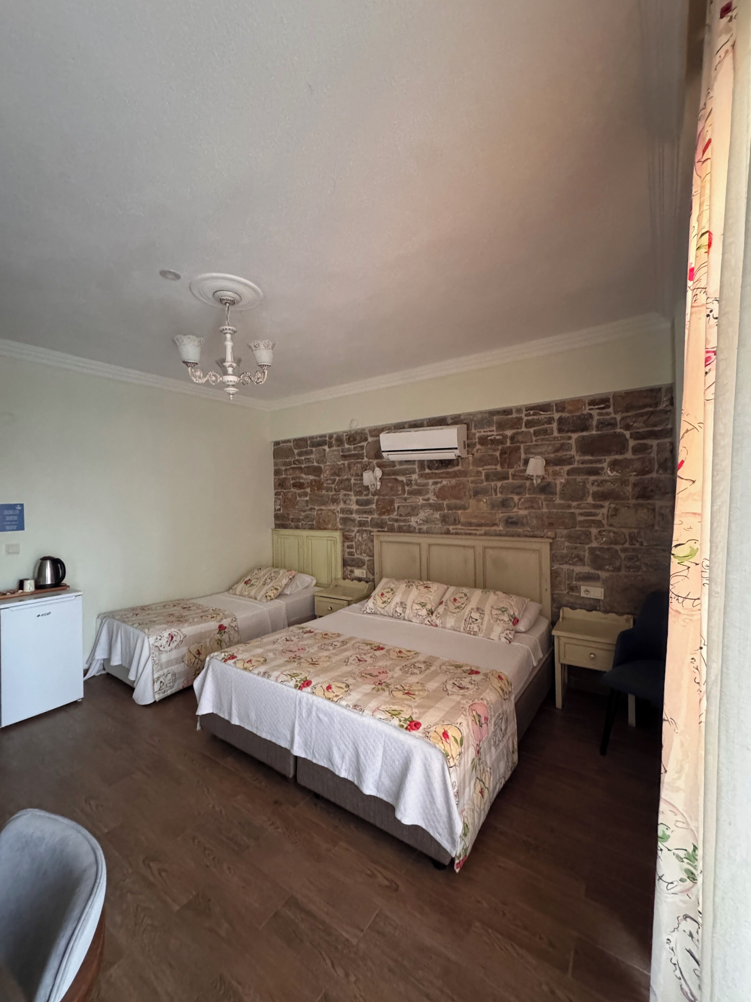 A hotel room with two beds, a small kitchenette, a stone accent wall, and a ceiling fan.