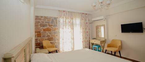 Un dormitorio con cama, dos sillas, escritorio, televisión y pared de piedra.