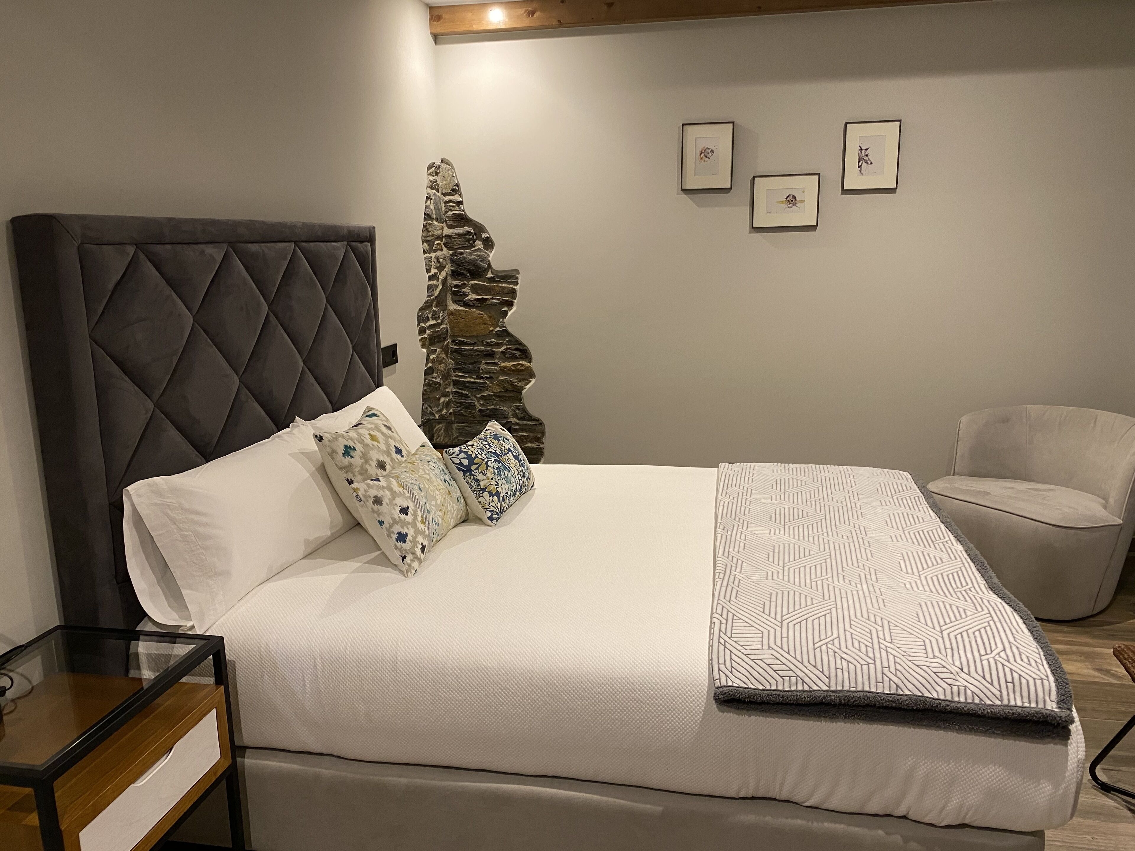 Un dormitorio ordenado con una cama grande, una mesita de noche, una silla y una pared con tres cuadros enmarcados.