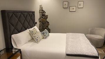 Un dormitorio ordenado con una cama grande, una mesita de noche, una silla y una pared con tres cuadros enmarcados.