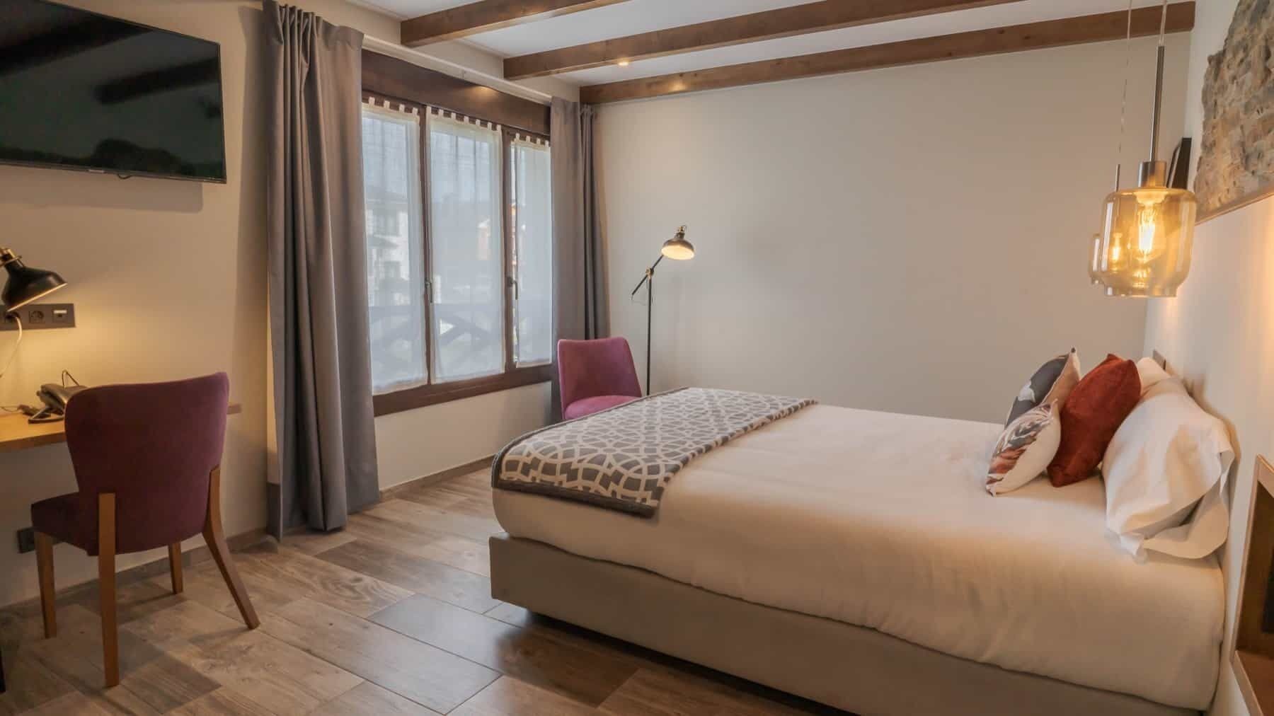 A bedroom with a large bed, a desk, a chair, a lamp, and a TV.
