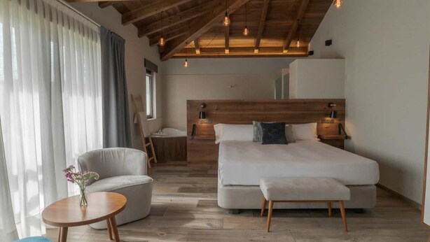 Un dormitorio con una cama grande, una mesita de noche, una silla y una pequeña mesa redonda con flores.