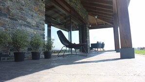 Un espacio al aire libre techado con paredes de piedra, suelo de hormigón y dos sillones de descanso.