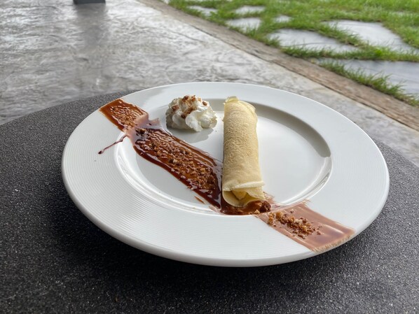 Un plato de postre con un crepé enrollado, una bola de helado y un hilo de salsa de chocolate.