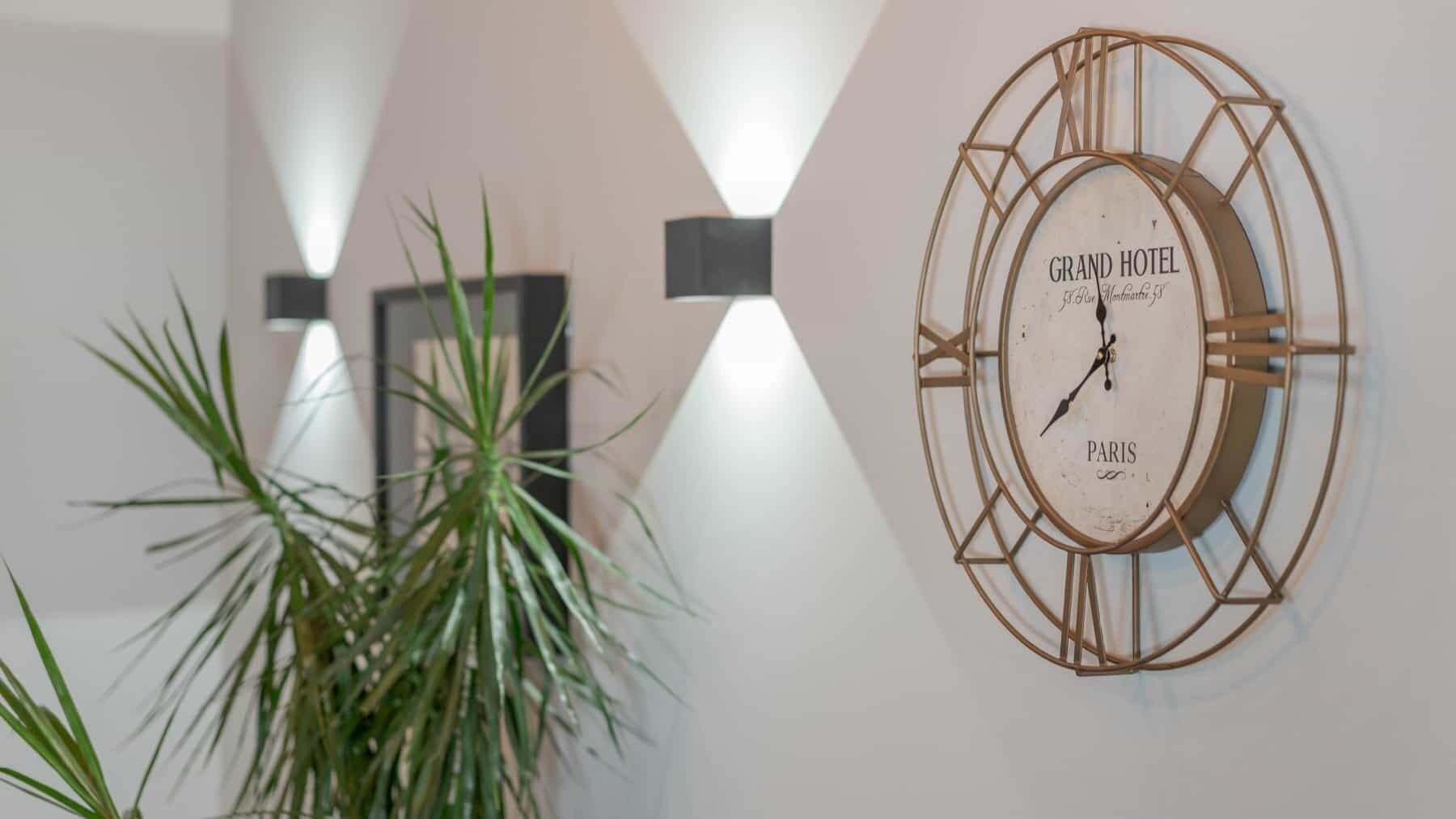 A wall-mounted clock with "GRAND HOTEL PARIS" and "B&B Montmartre 3" on it, a potted plant, and a modern light fixture.