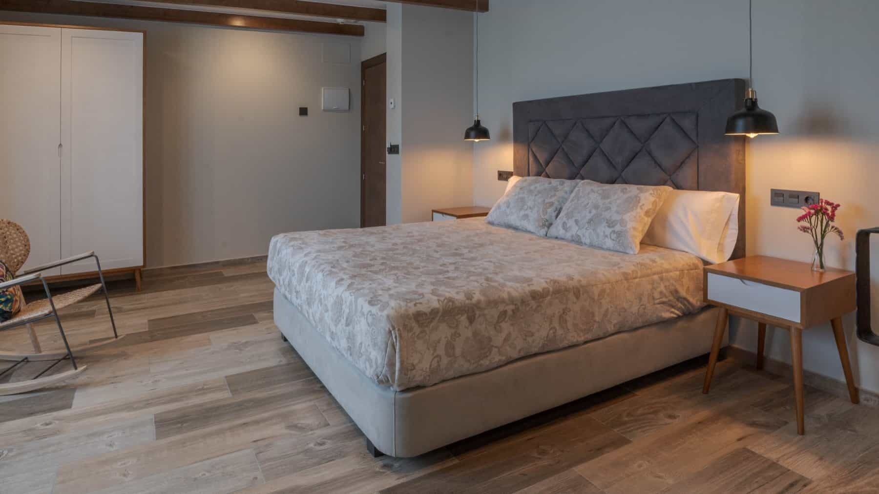 A bedroom with a bed, two bedside tables, a chair, and a wooden floor.