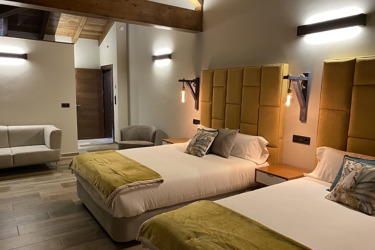 A hotel room with two beds, a sofa, and a wooden ceiling.