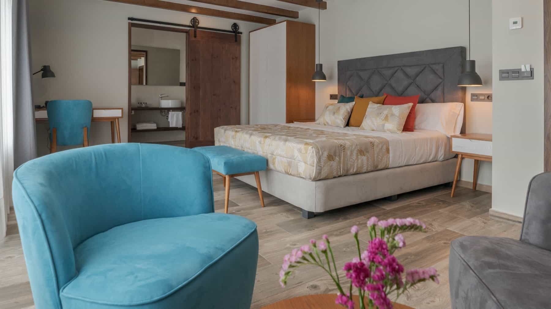 A modern bedroom with a large bed, a blue armchair, and a wooden floor.