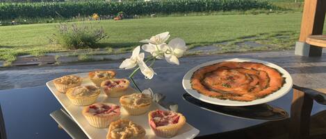 A table with a variety of pastries and a salmon tart, set against a scenic view of a vineyard and mountains.