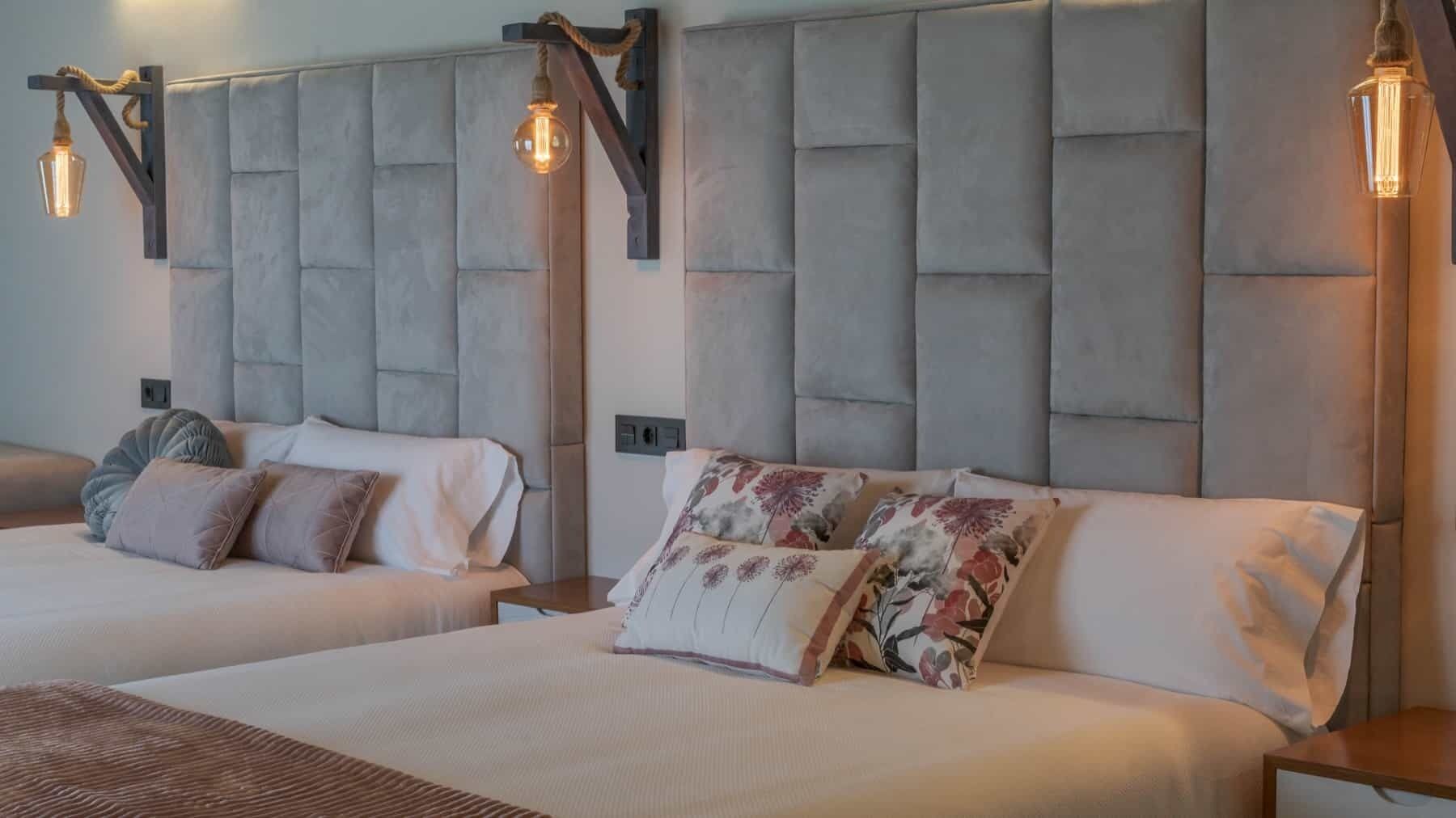 A hotel room with two beds, each with a tufted headboard and bedside lamps.
