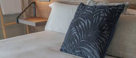 A bed with a white mattress, a dark blue pillow with a leaf pattern, and a grey textured pillow.