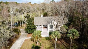 A two-story house with a front porch, surrounded by trees and a paved driveway.