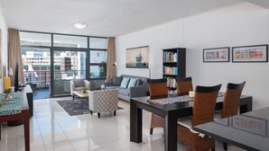 Una sala de estar moderna con comedor, ventanas grandes, una estantería y un sofá.