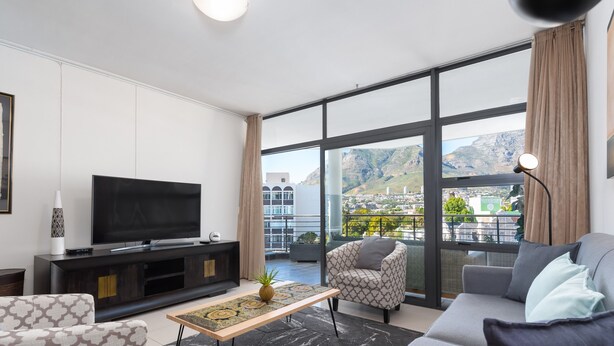 Una sala de estar moderna con un televisor grande, asientos cómodos, una mesa de centro y vistas a la ciudad y a las montañas a través de grandes ventanales.