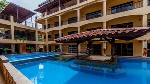 Ein mehrstöckiges Hotel mit einem zentralen Pool, Balkonen und einem überdachten Bereich.