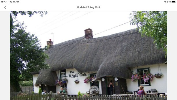Un pub tradicional con techo de paja llamado 'The Royal Oak' y una valla de madera al frente.
