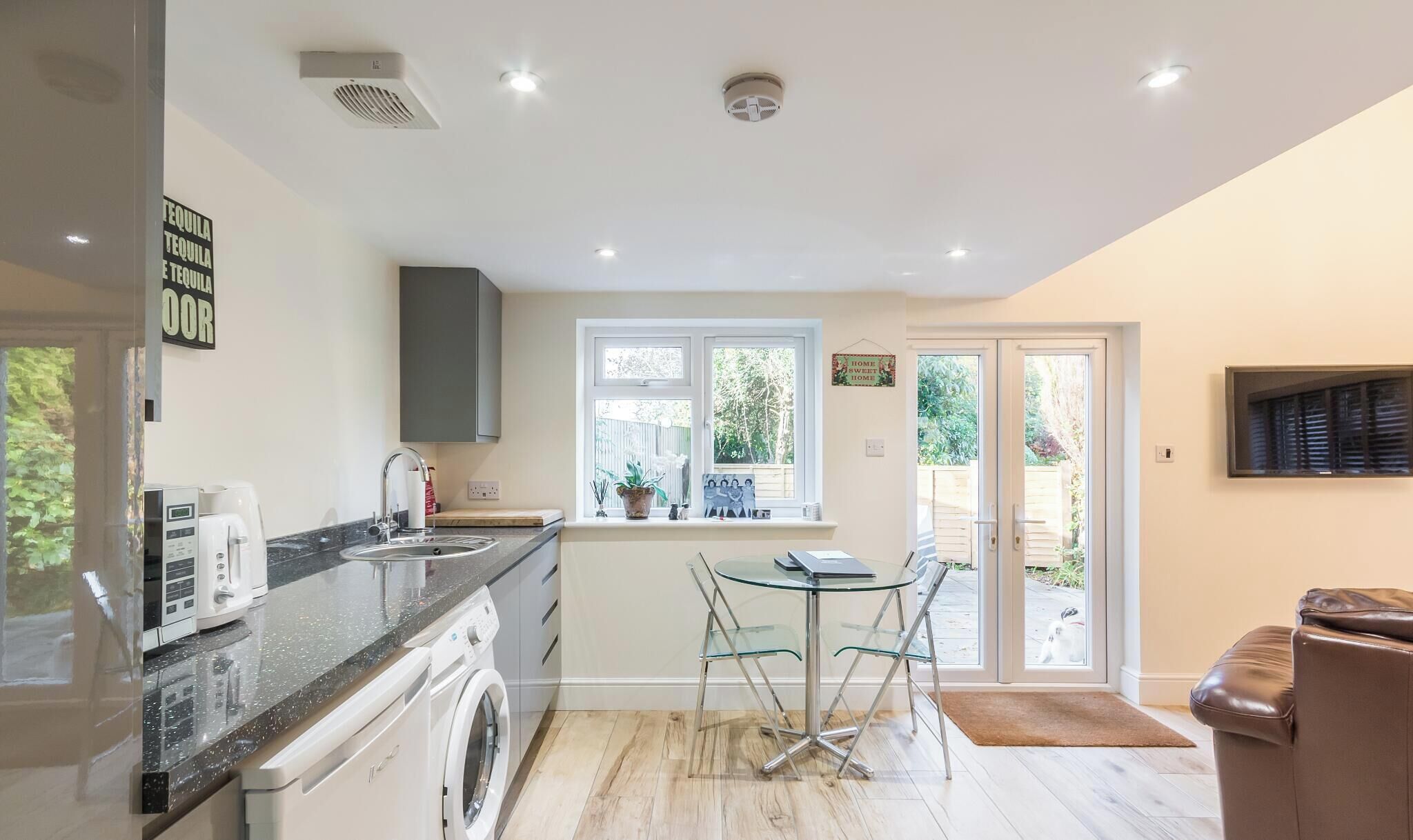 A modern kitchen with a washing machine, a coffee maker, and a dining area with a table and chairs.